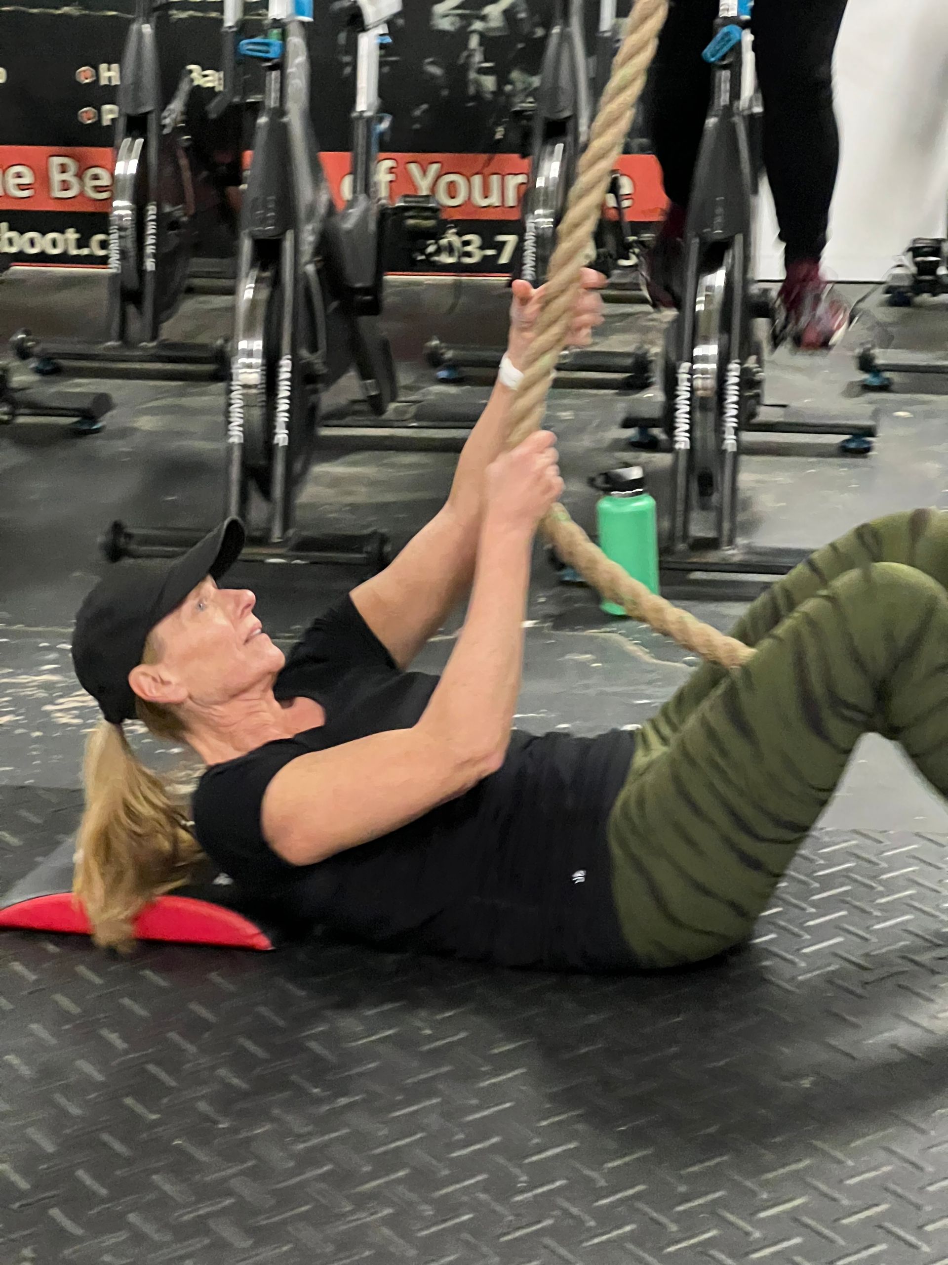A woman is laying on the floor holding a rope in a gym