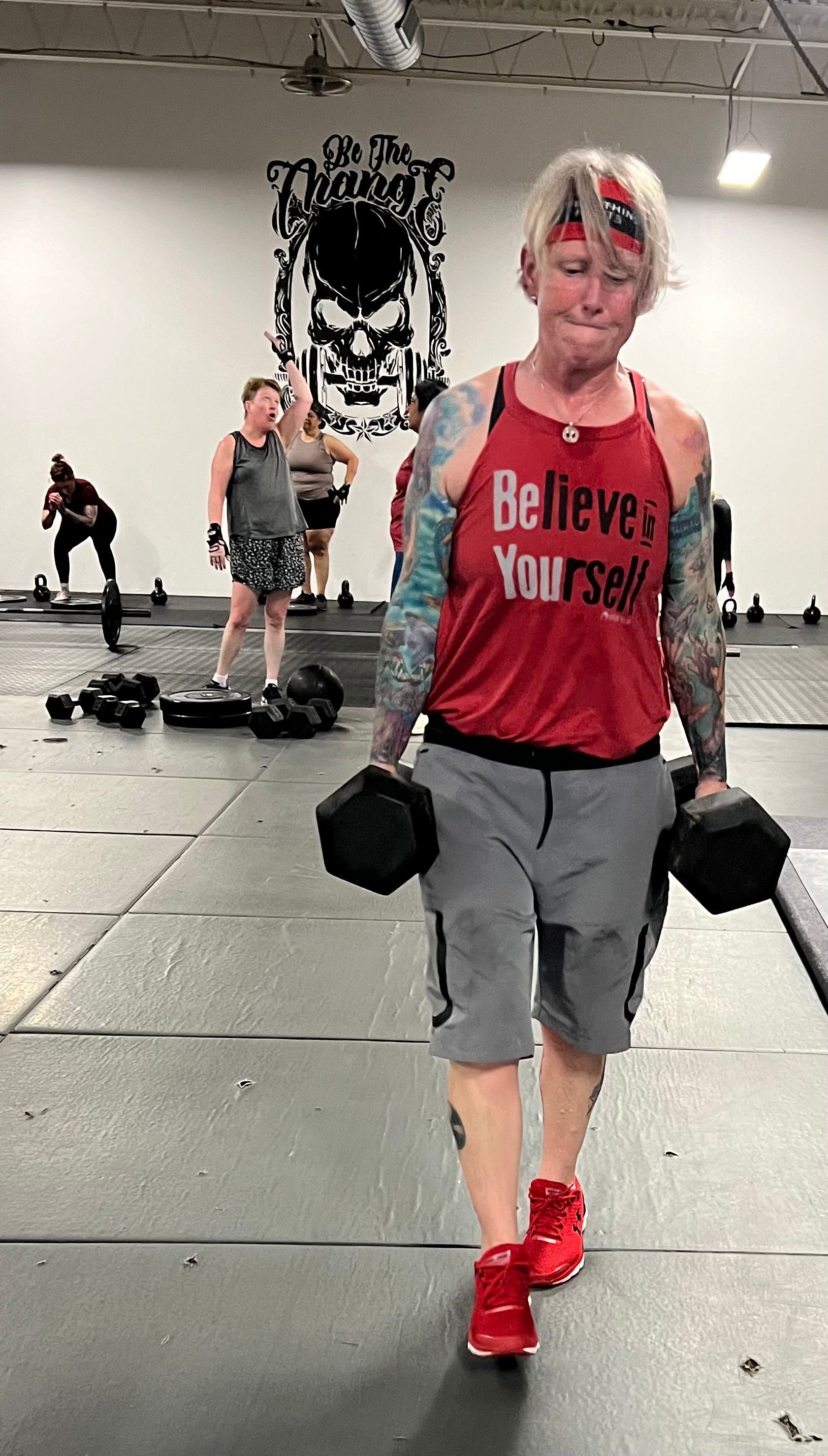 A woman in a red tank top is carrying dumbbells in a gym.