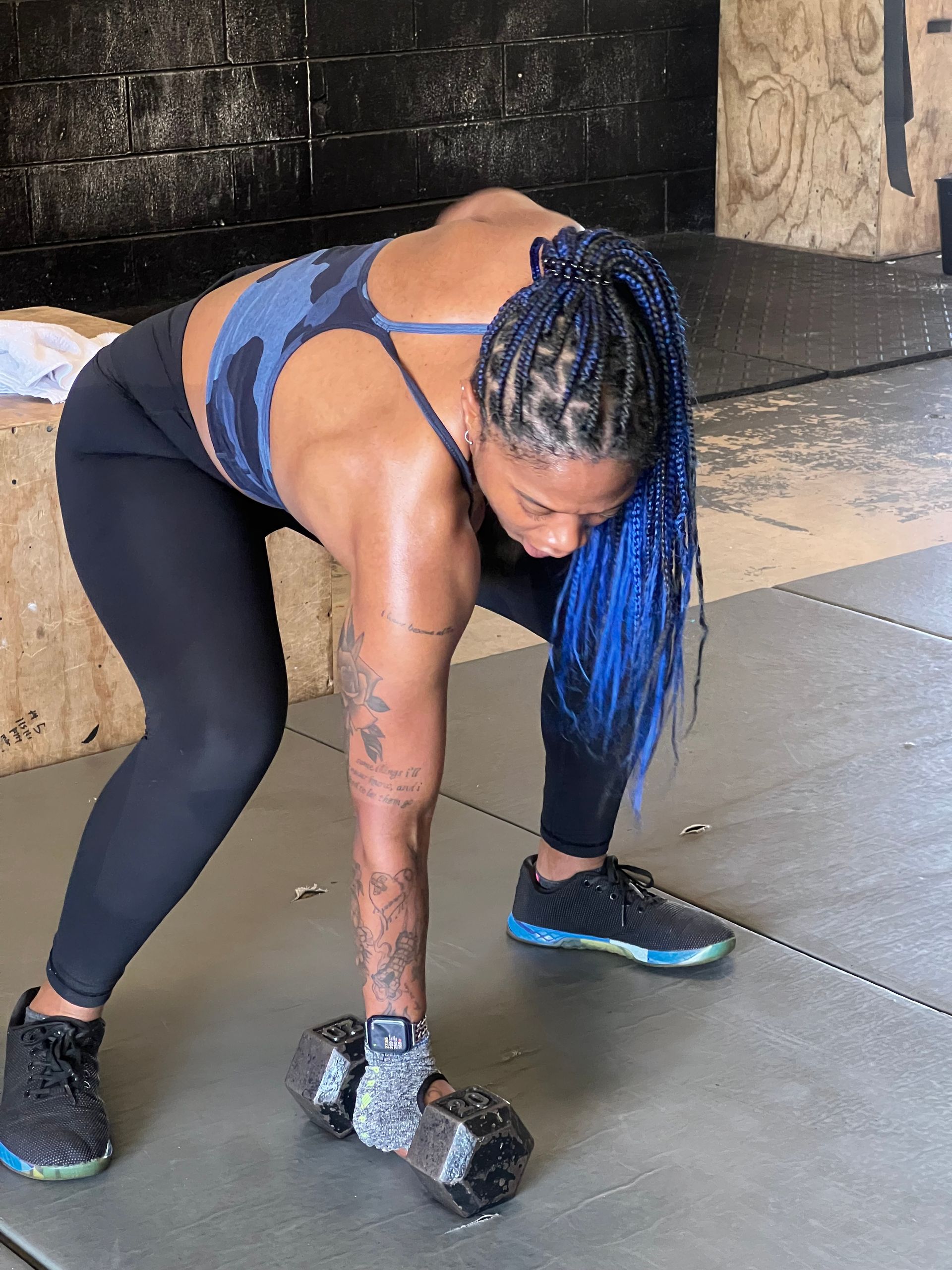 A woman with blue hair is holding a dumbbell in her hand.