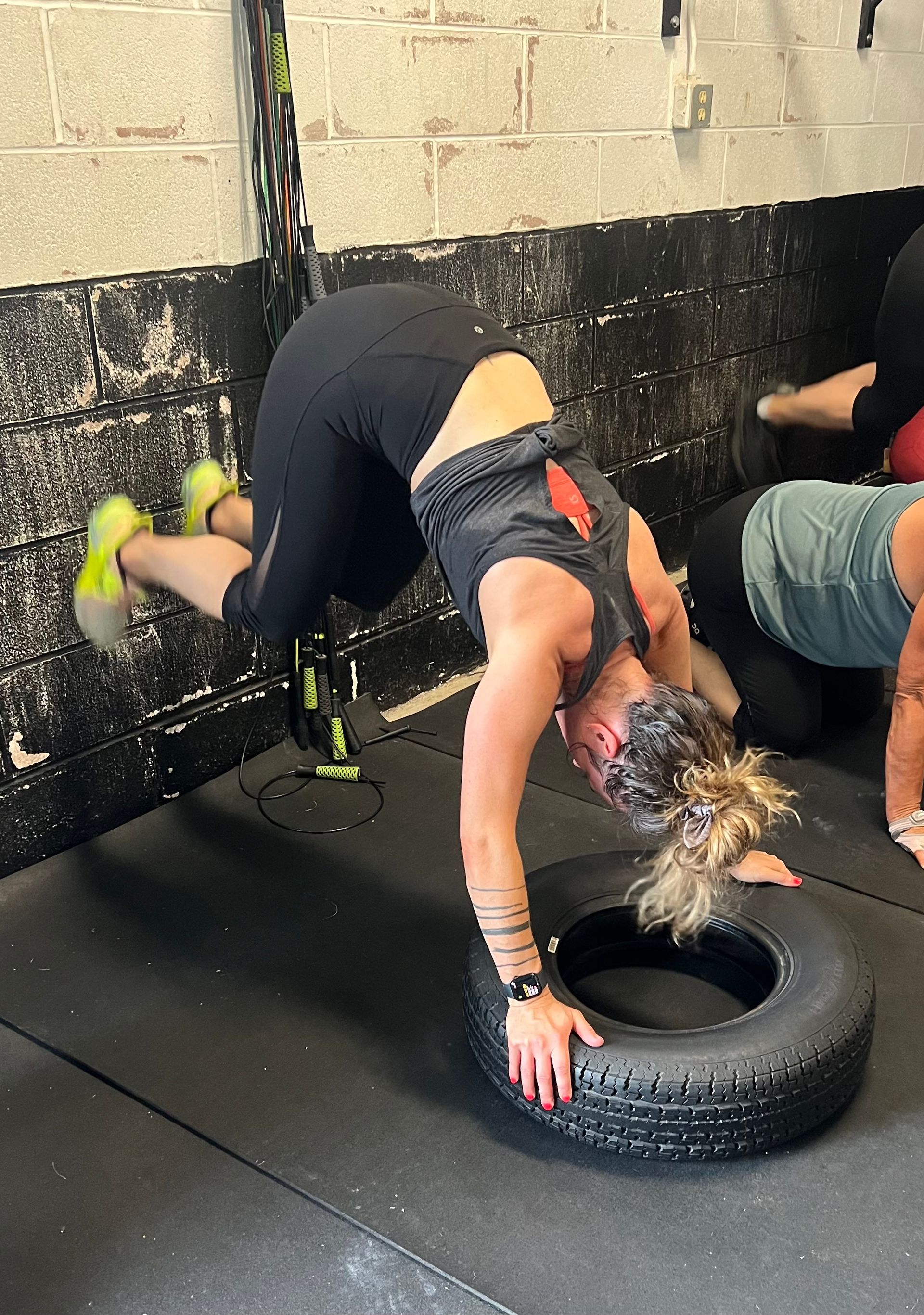A woman is doing a handstand on a tire in a gym.