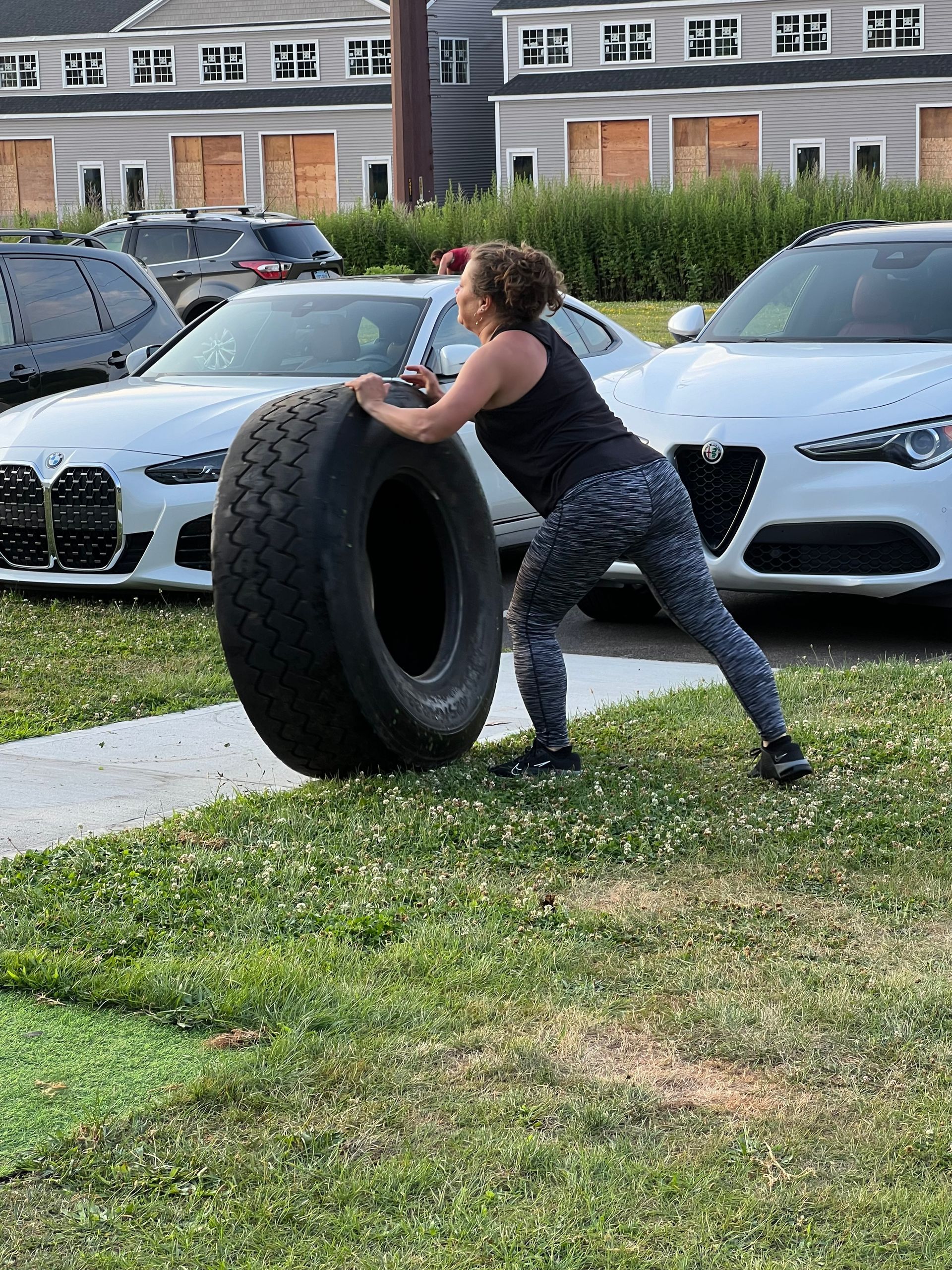 A woman is pushing a large tire in a parking lot.