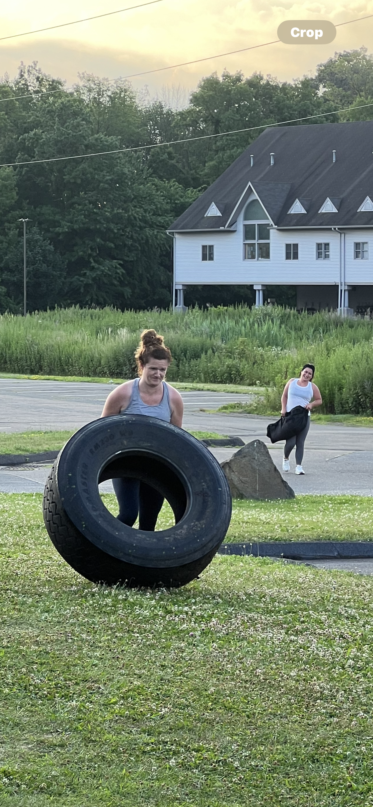 A woman is pushing a large tire in a field.