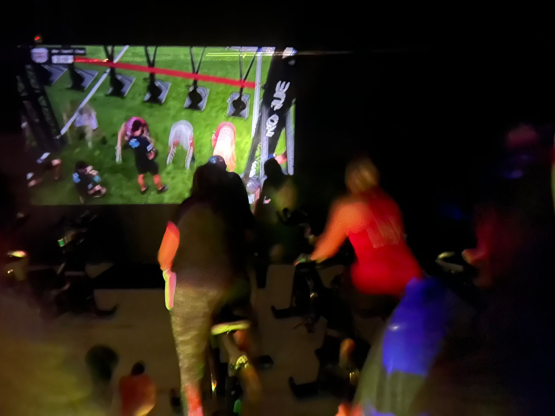 A group of people are riding exercise bikes in front of a large screen.
