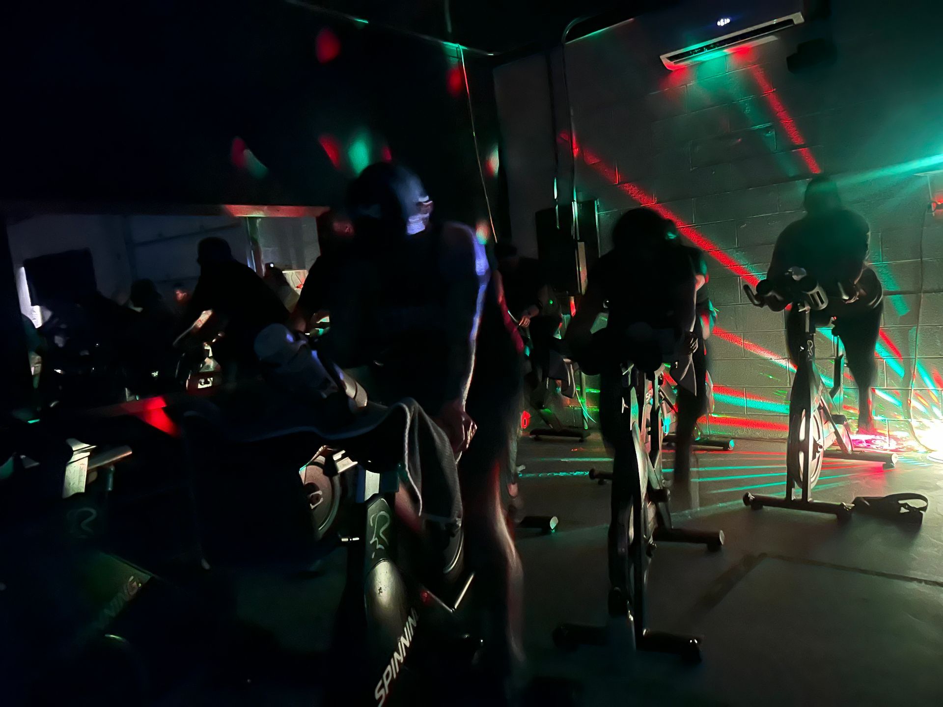 A group of people are riding exercise bikes in a dark room.