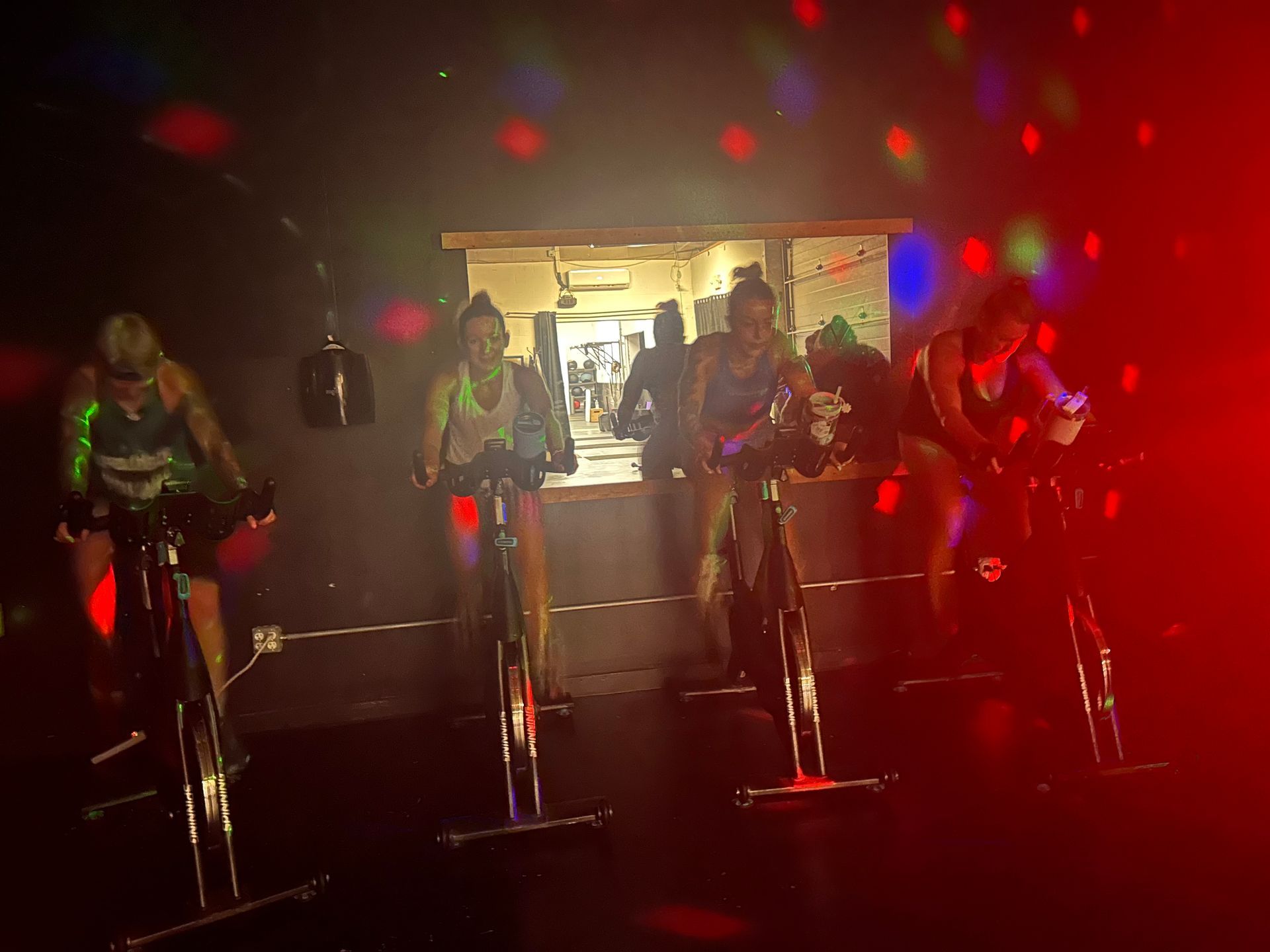 Five people standing on exercise bikes in a dark studio with colorful lights