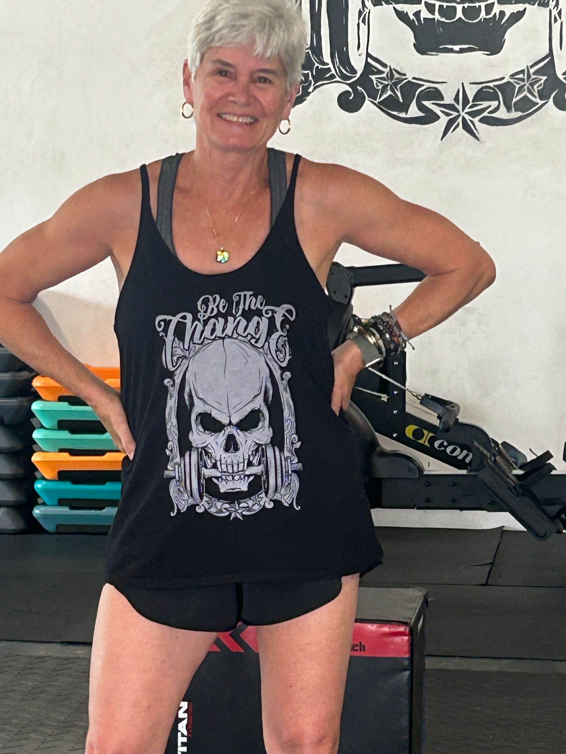 Smiling person in black tank top and shorts posing in a gym