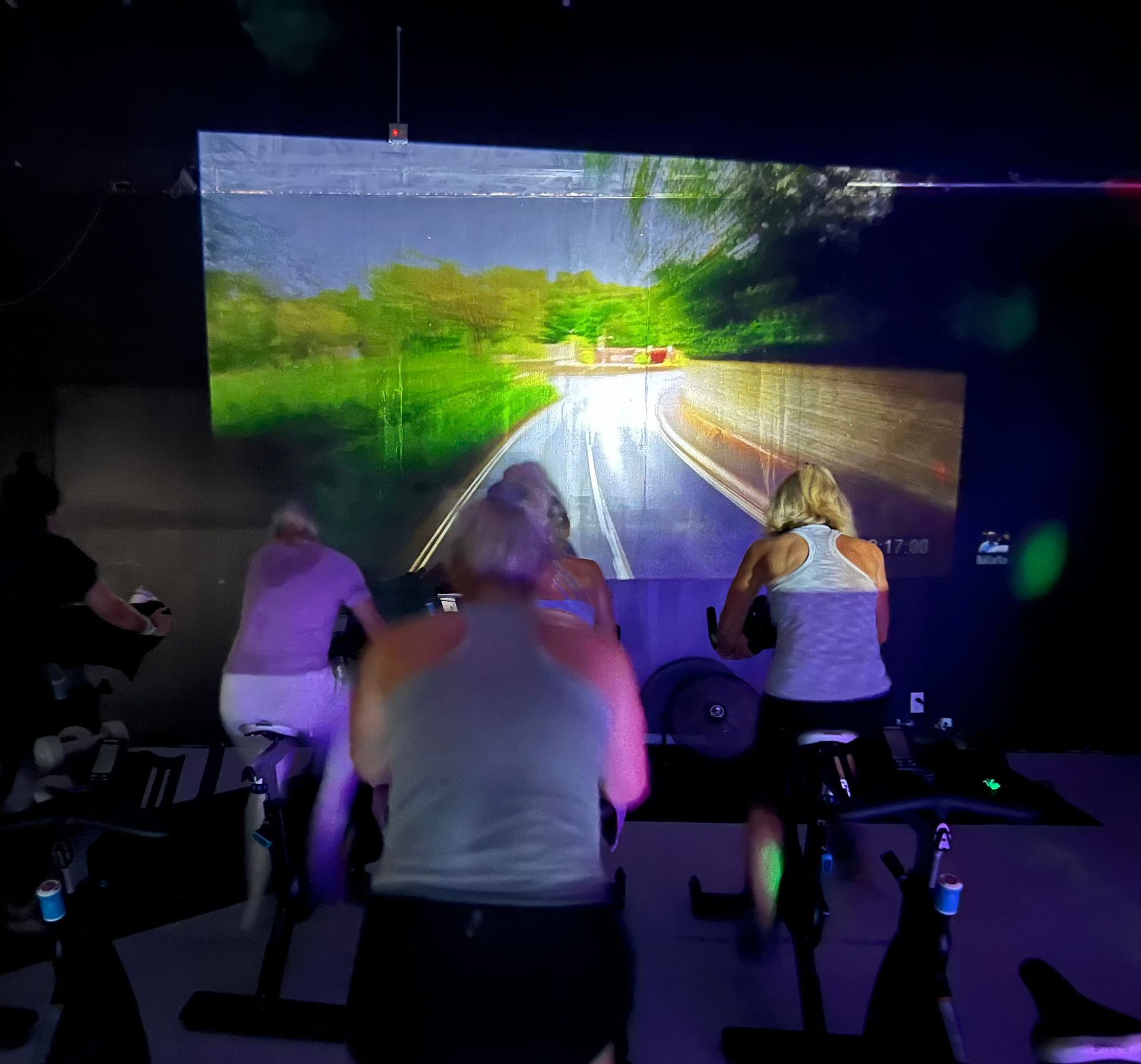 A group of people are riding exercise bikes in front of a large screen.