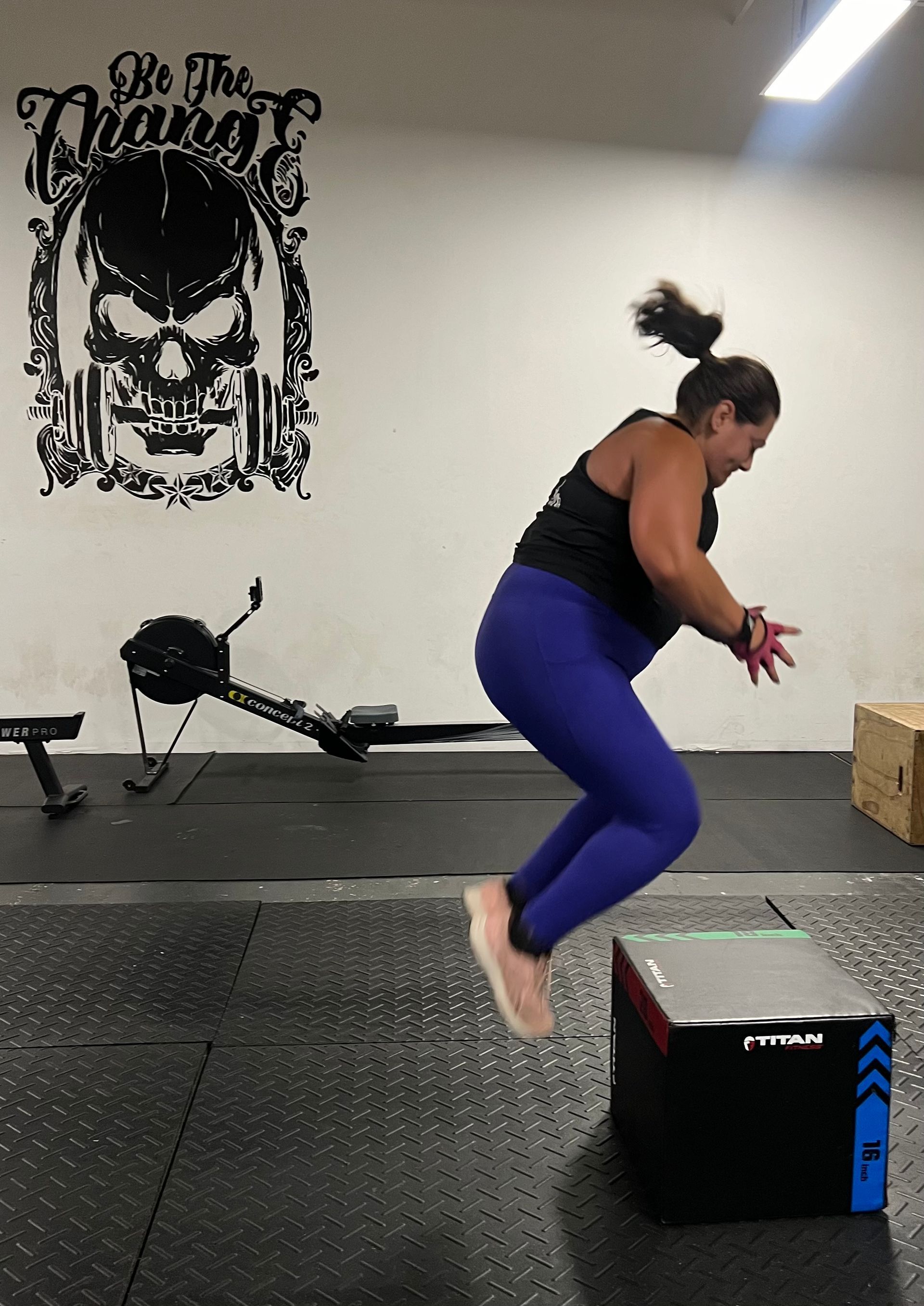 A woman is jumping over a box in a gym