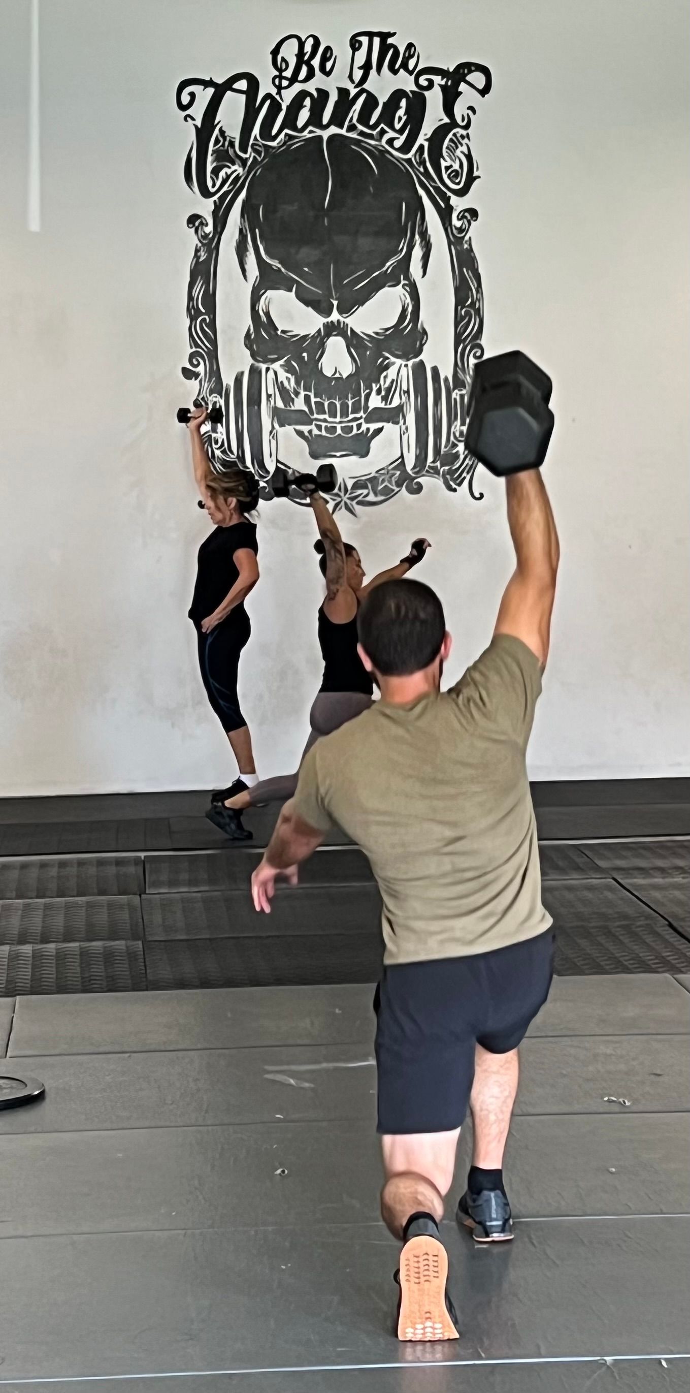 A man is lifting a dumbbell over his head in a gym.