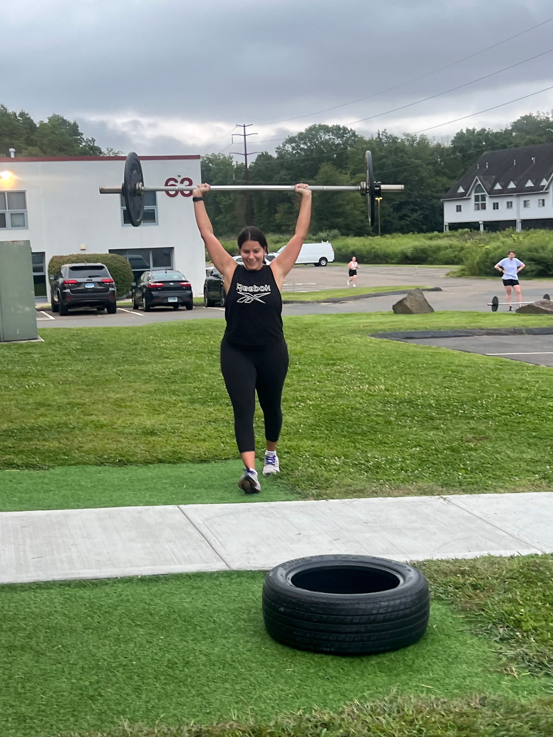 A woman is lifting a barbell over a tire.