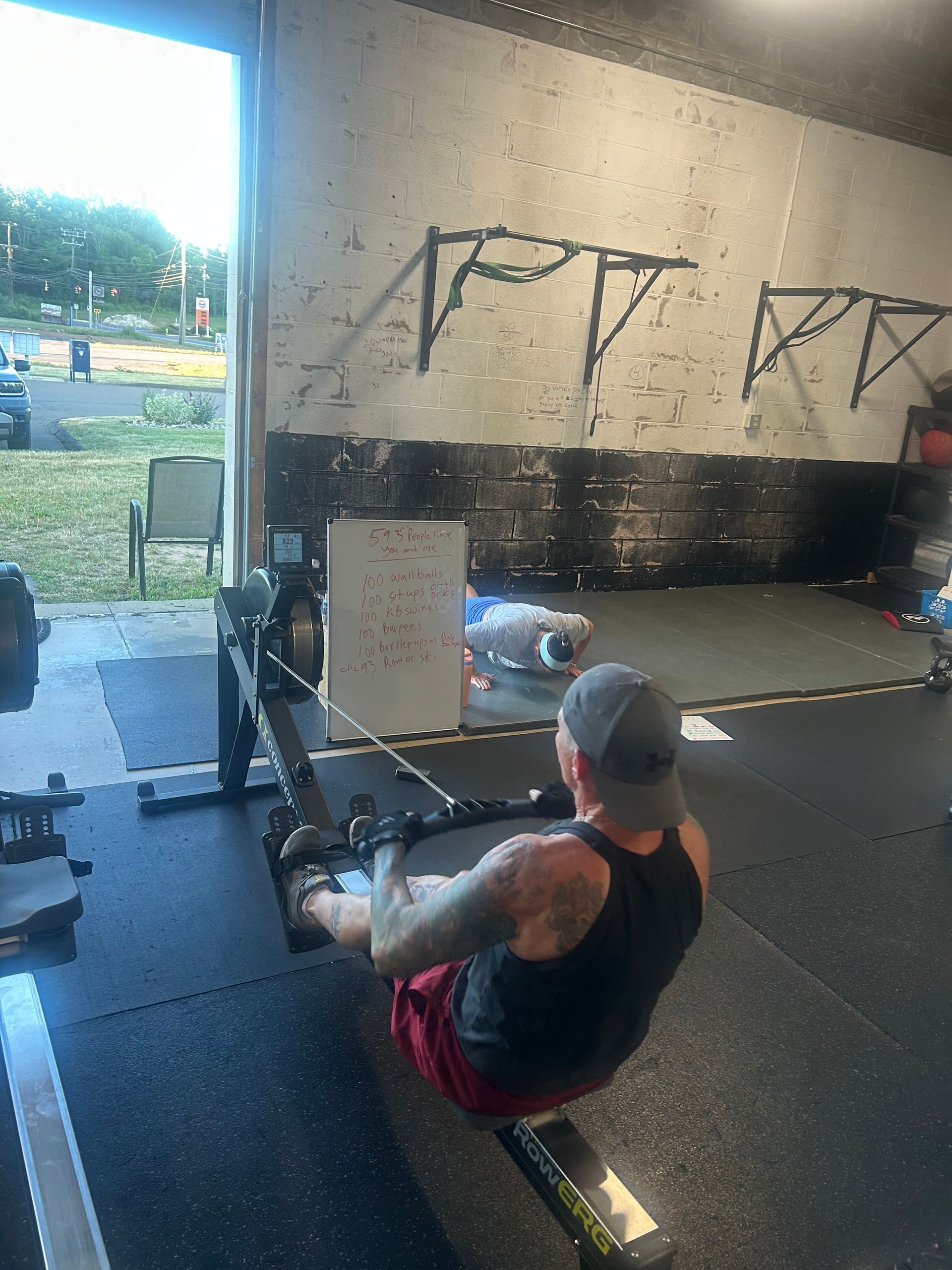 Person in a gym doing a seated rowing exercise on a machine, with weights and wall art in the background.