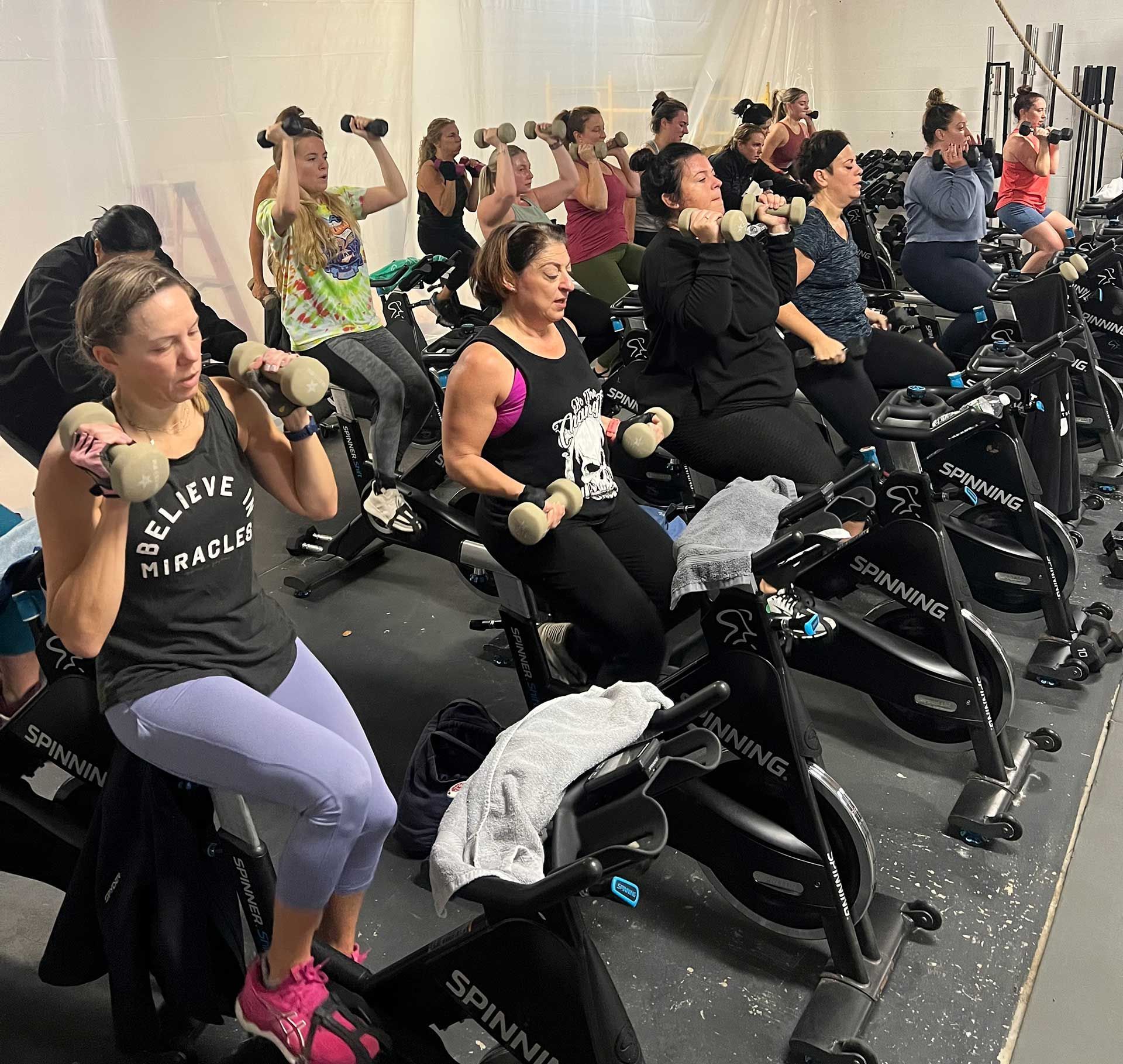 A group of women are riding exercise bikes and lifting dumbbells in a gym