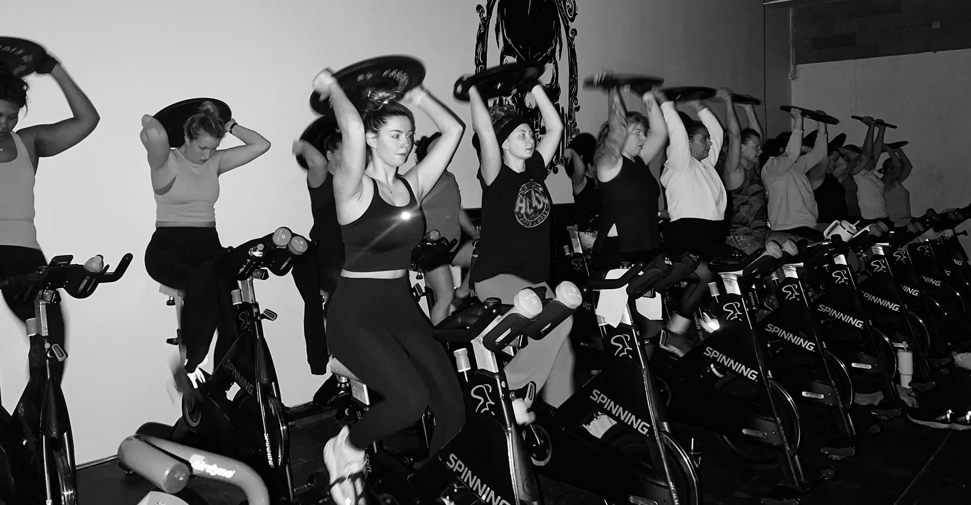A group of people are riding exercise bikes while lifting weights