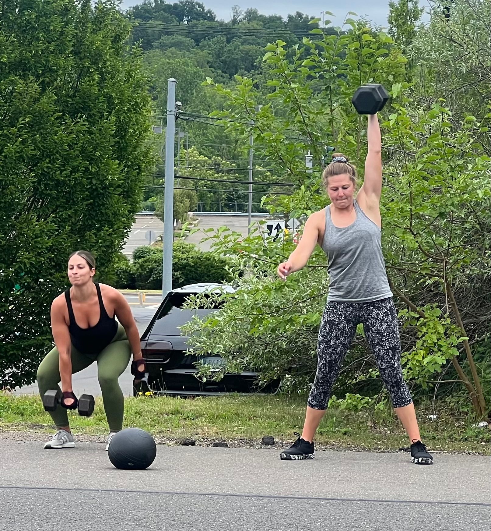 Two women are doing exercises with dumbbells on the side of the road.