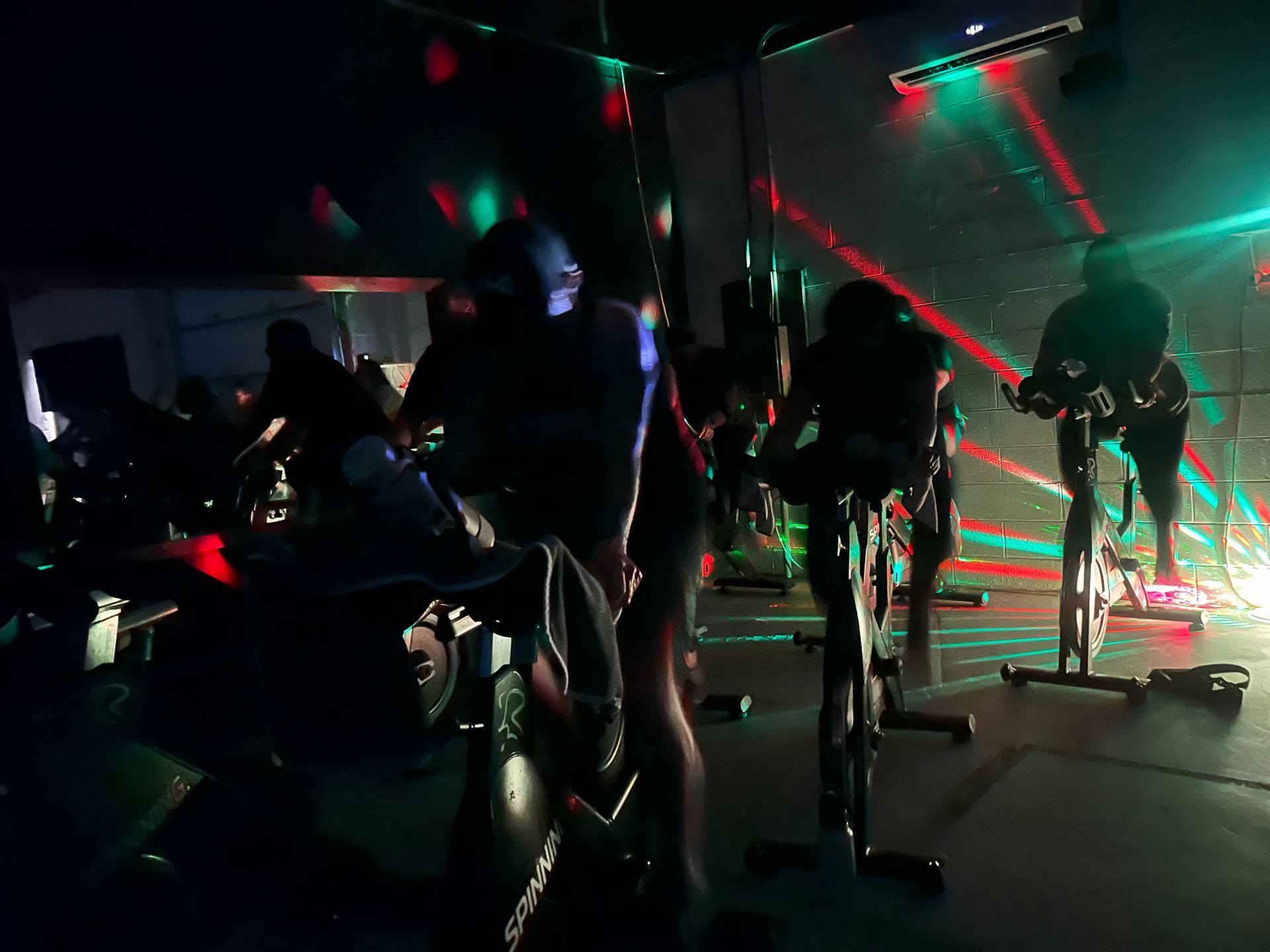 A group of people are riding exercise bikes in a dark room.