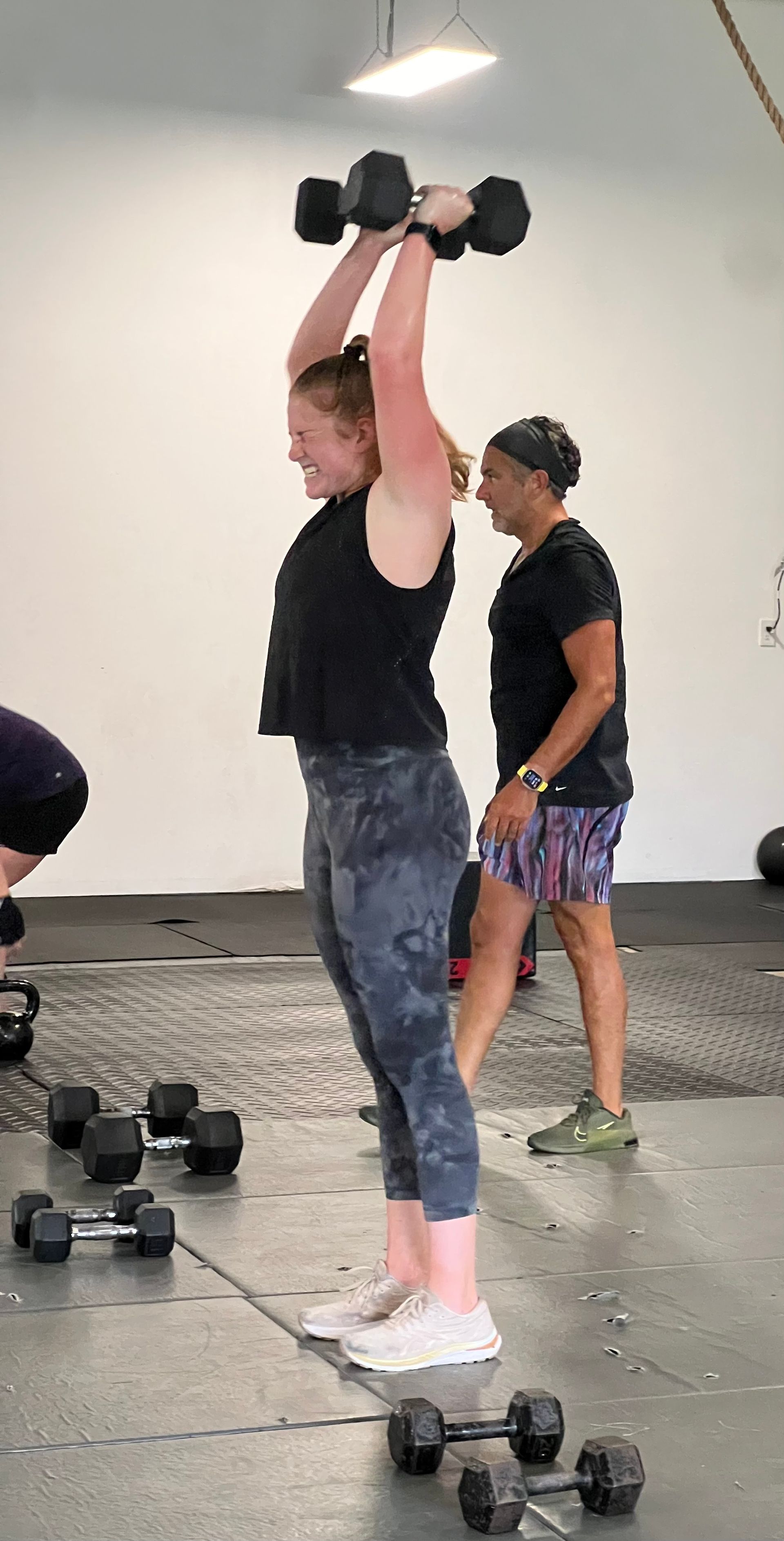 A woman is lifting a dumbbell over her head in a gym.