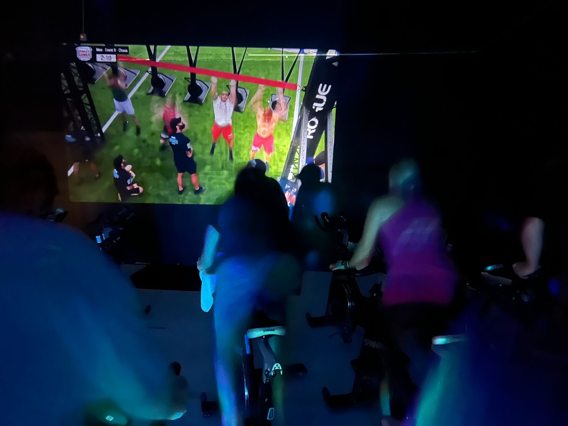 A group of people are riding bikes in front of a large screen.