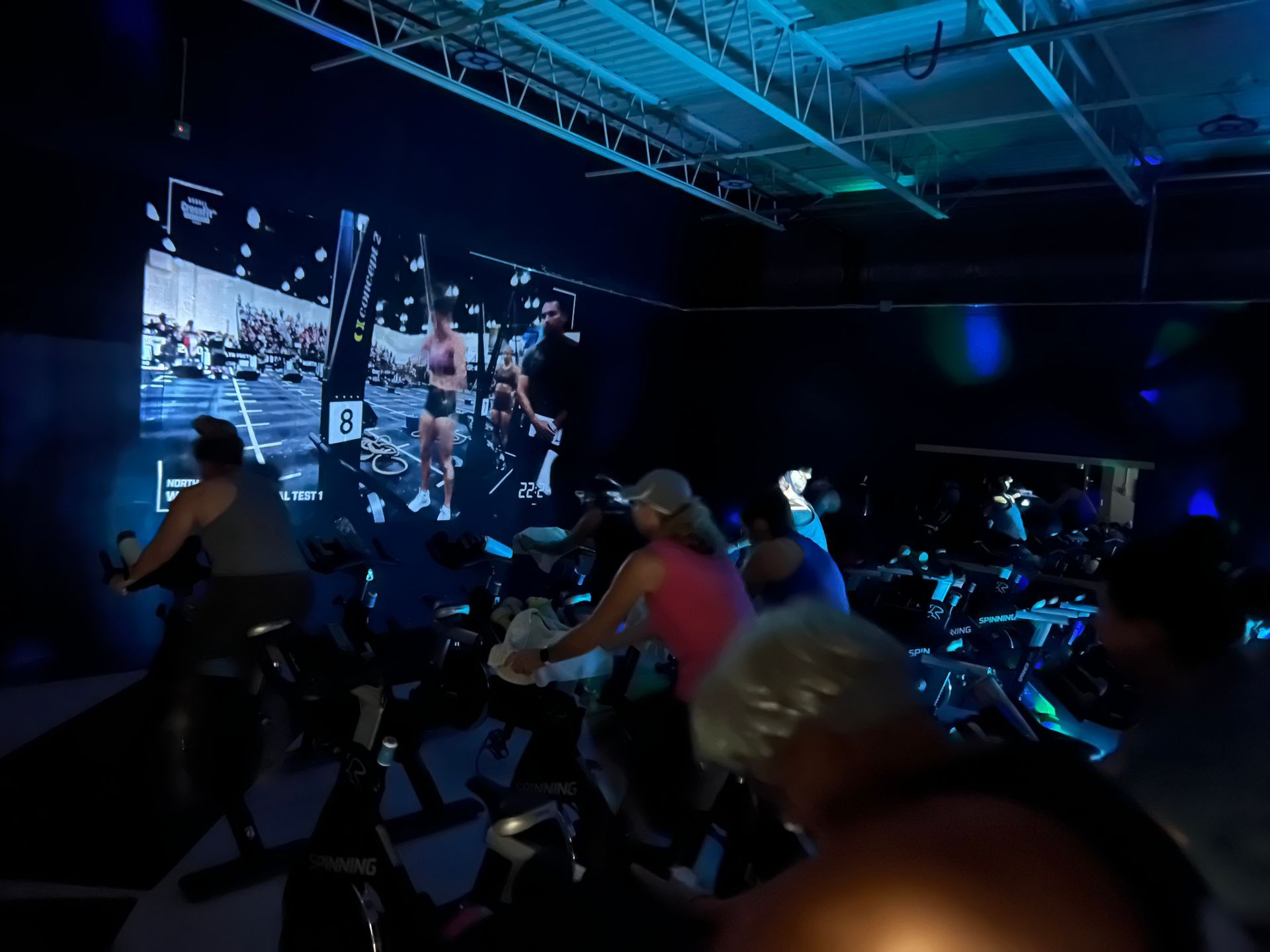 A group of people are riding exercise bikes in front of a large screen.
