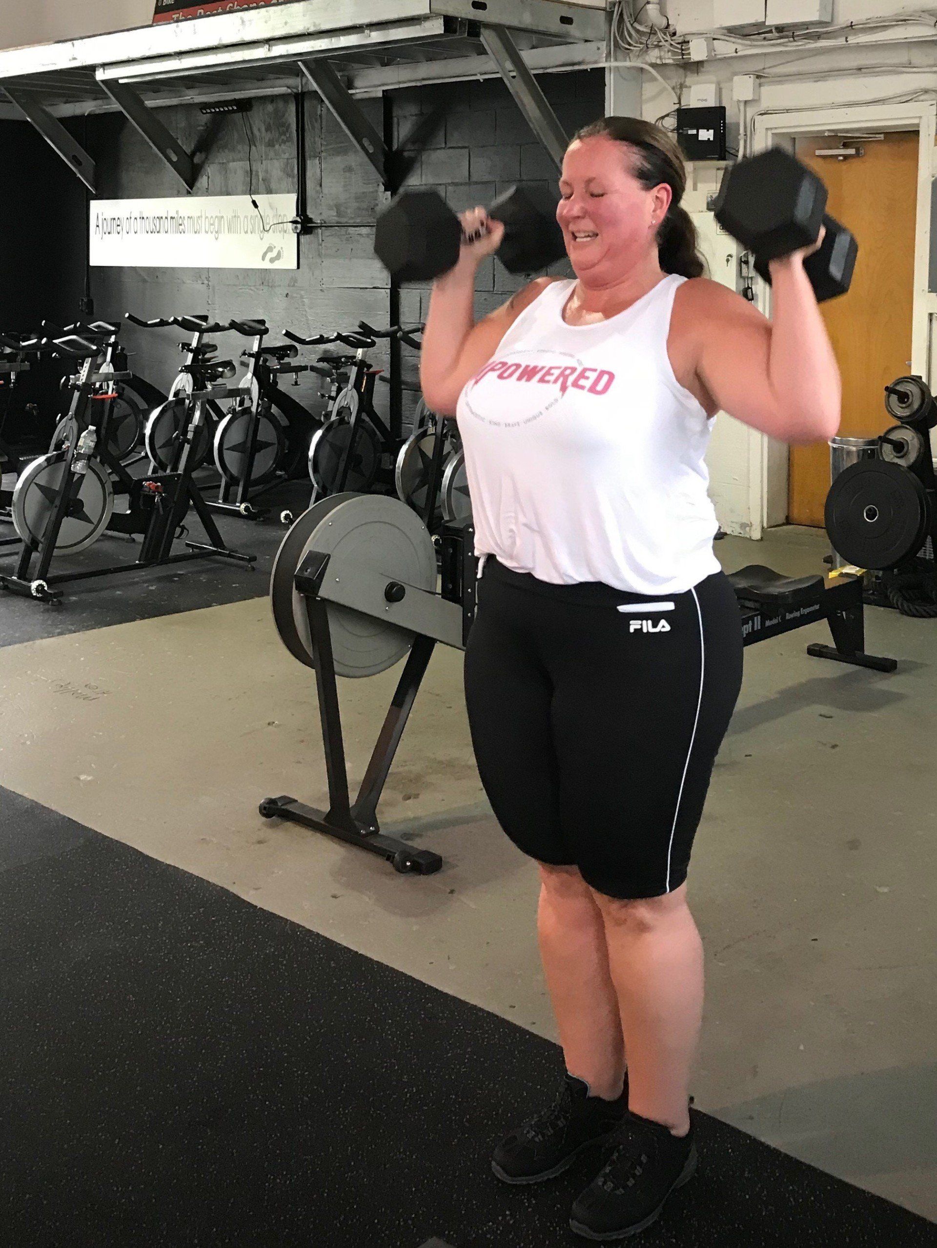 A woman is lifting dumbbells in a gym.