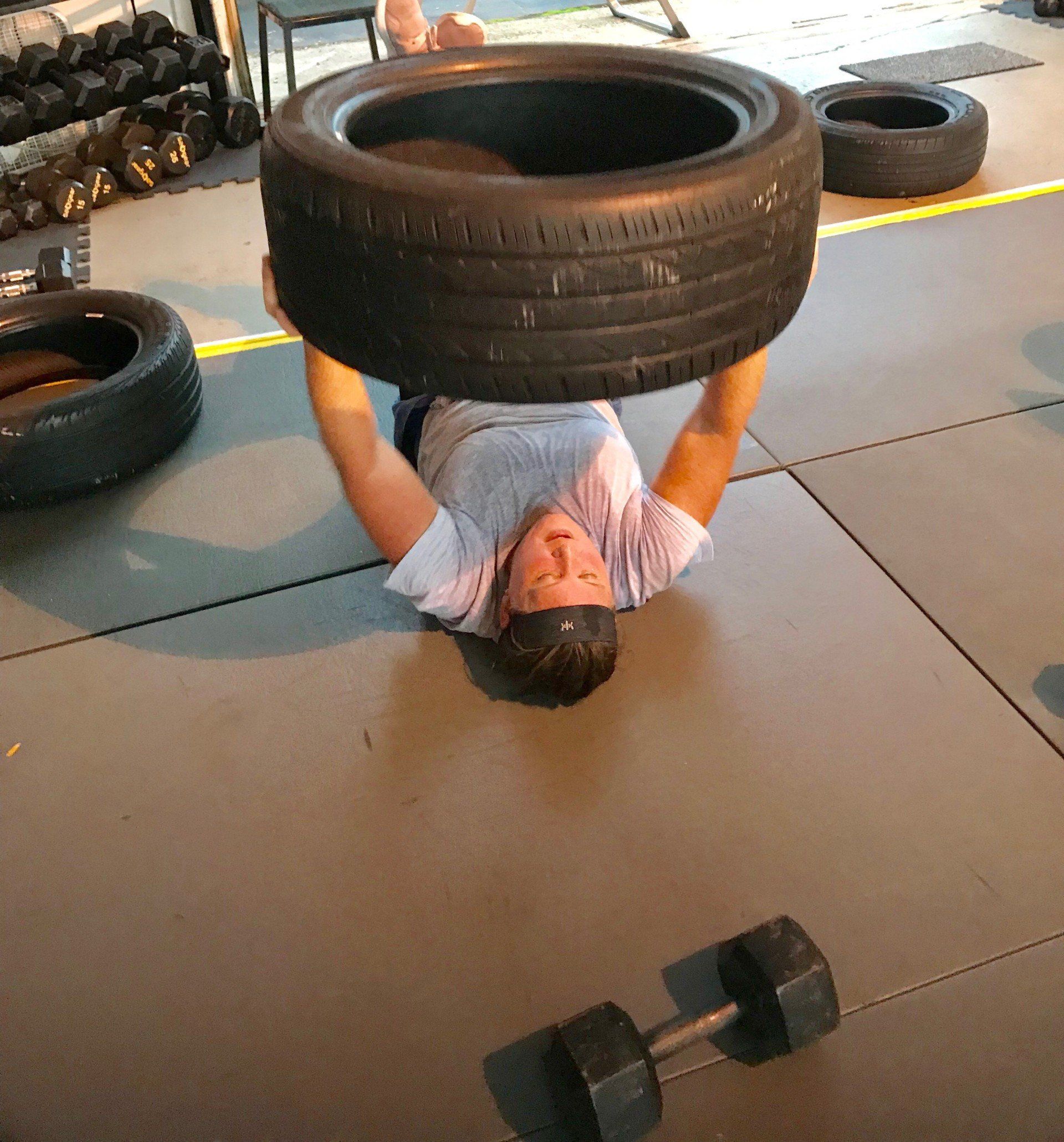 A man is laying on his back holding a tire over his head