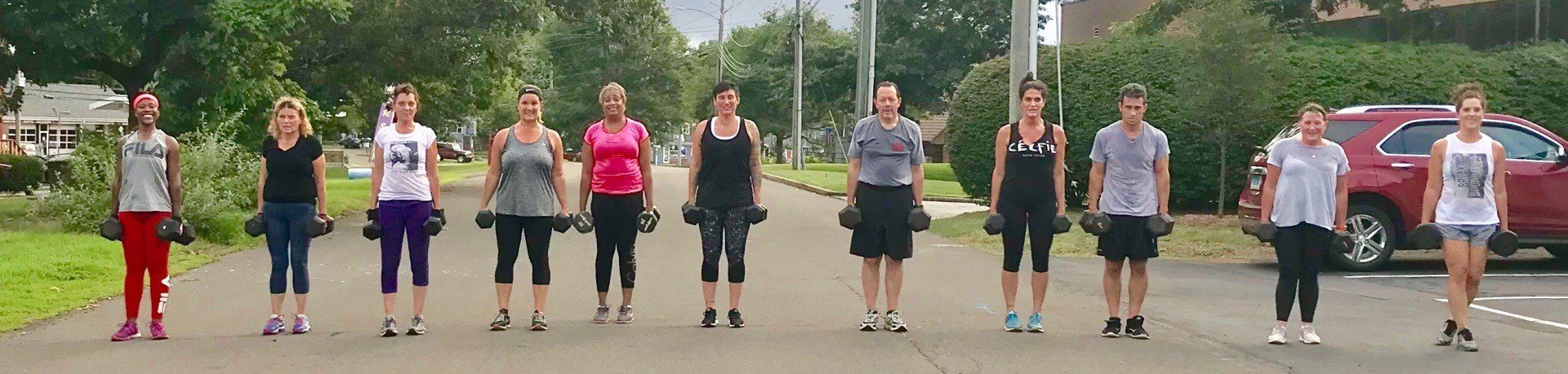 A group of people are standing in a row on a street holding dumbbells.