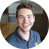Man with brown hair, smiling, wearing a gray polo shirt, indoors.