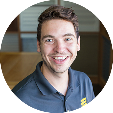 Man with brown hair, smiling, wearing a gray polo shirt, indoors.