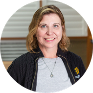 Woman with blonde hair, smiling, wearing a gray shirt and black jacket.