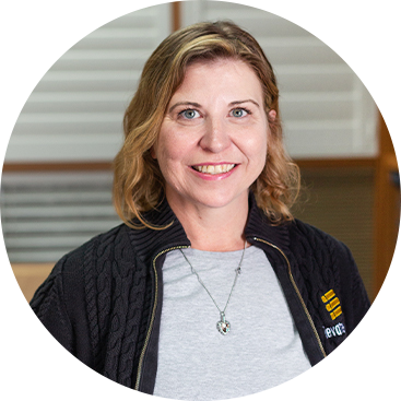 Woman with blonde hair, smiling, wearing a gray shirt and black jacket.