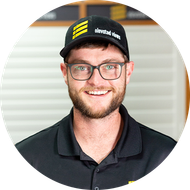 Man wearing glasses and a hat with a logo, smiling, indoors.