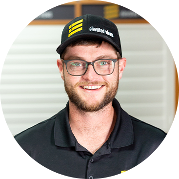 Man wearing glasses and a hat with a logo, smiling, indoors.