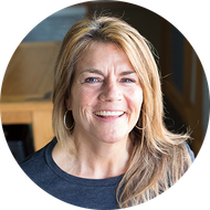 Woman with blonde hair smiles, wearing hoop earrings and a dark gray shirt.