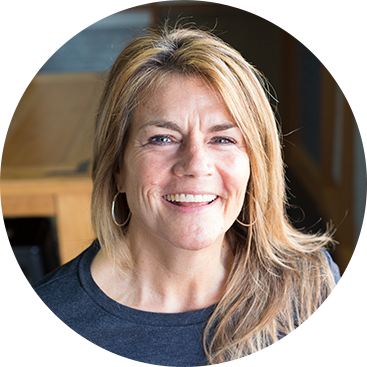 Woman with blonde hair smiles, wearing hoop earrings and a dark gray shirt.