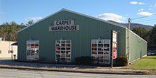 Green Carpet Warehouse building with sign, windows, and mountain background.