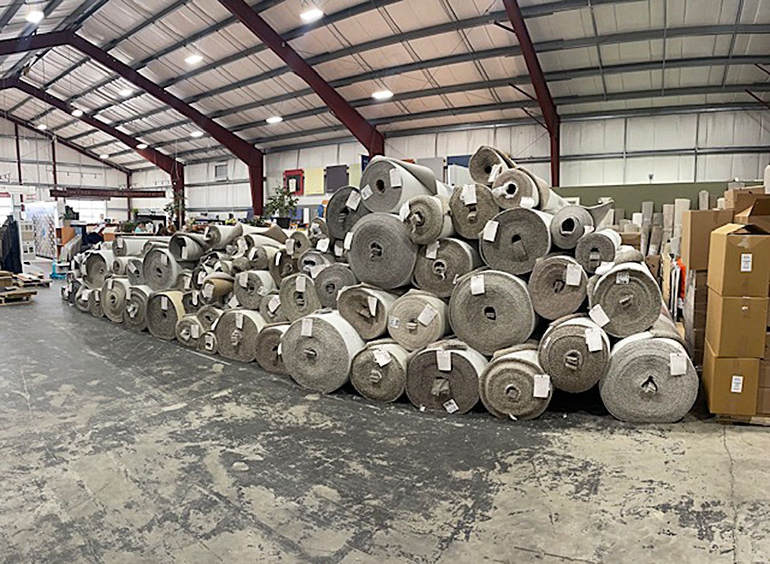 Large warehouse interior with many rolls of carpet stacked on the floor.