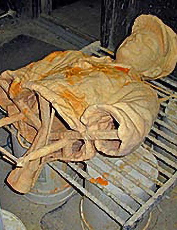 A clay sculpture of a torso and head wearing a cap, resting on a metal drying rack in a workshop.