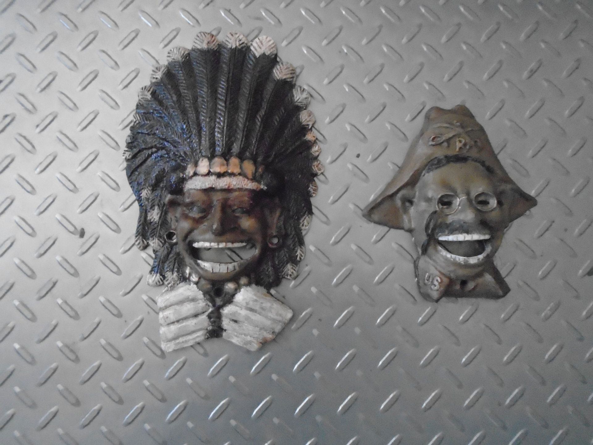 Two wall-mounted decorative masks, one featuring a headdress and one a pirate hat, on a metallic diamond-plate background.