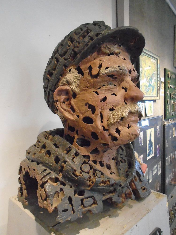 A textured, terracotta-colored bust of a person wearing a cap, featuring intricate, lace-like perforated patterns.