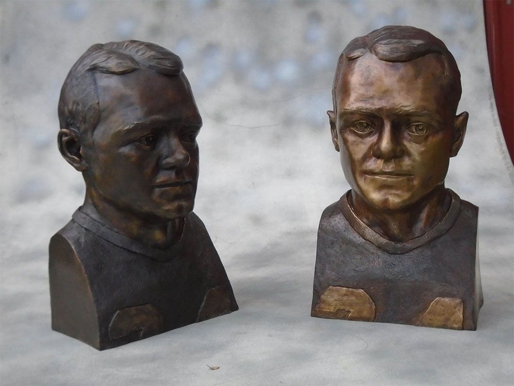 Two bronze busts of men in football jerseys, one facing right and the other facing forward, set against a light background.