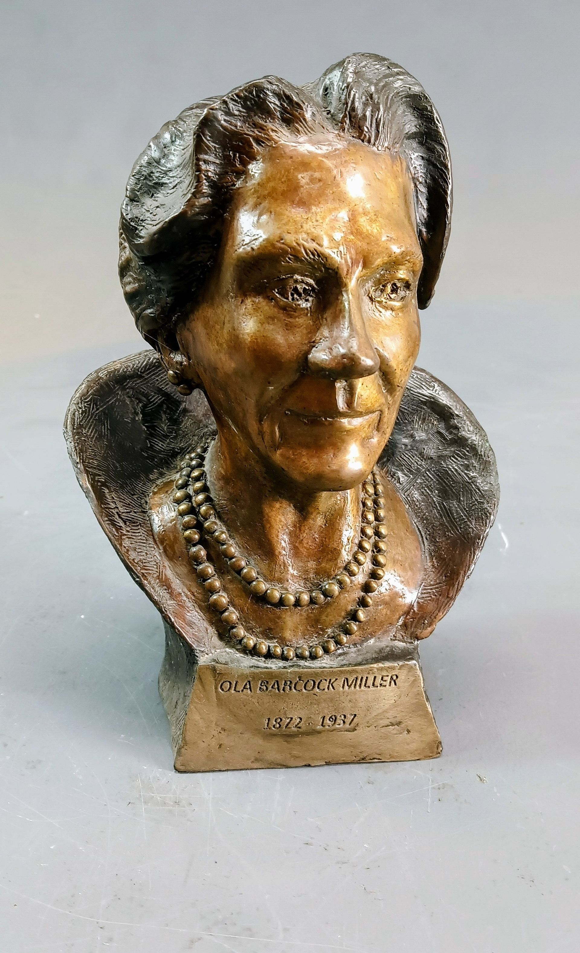 Bronze bust sculpture of a smiling person on a small pedestal