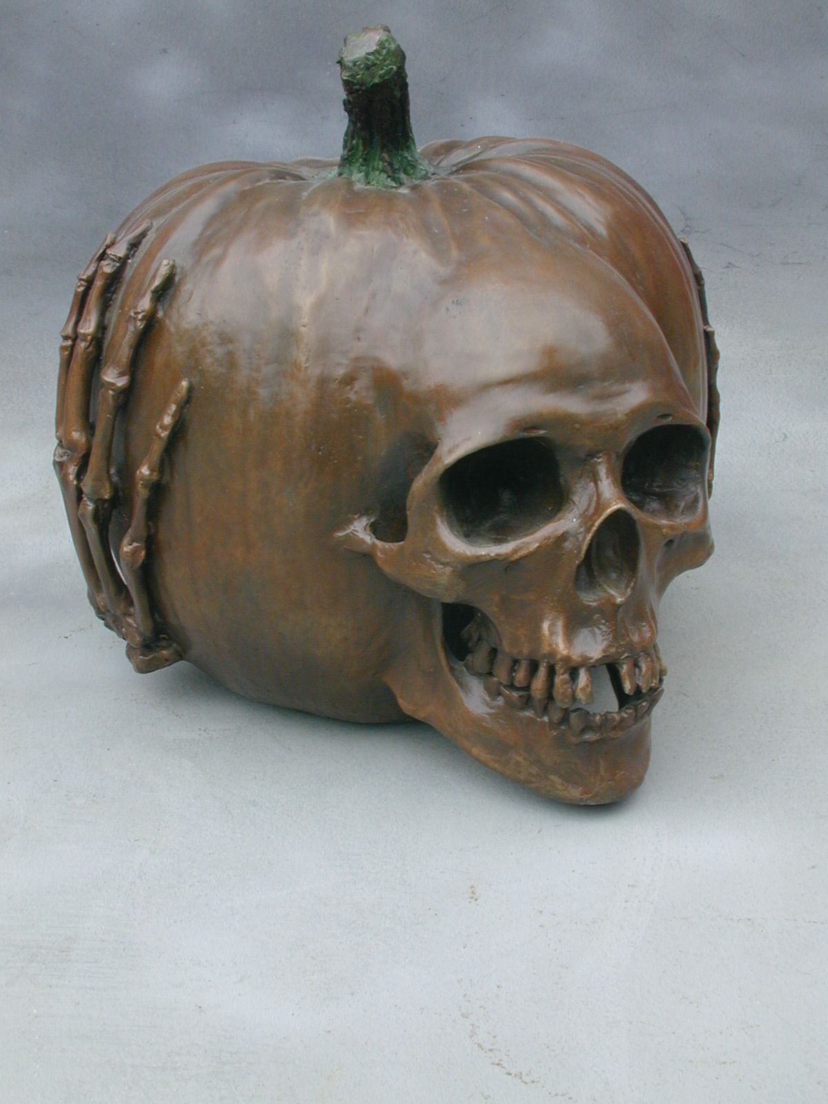 Bronze skull sculpture integrated into a pumpkin shape, with a green stem on top