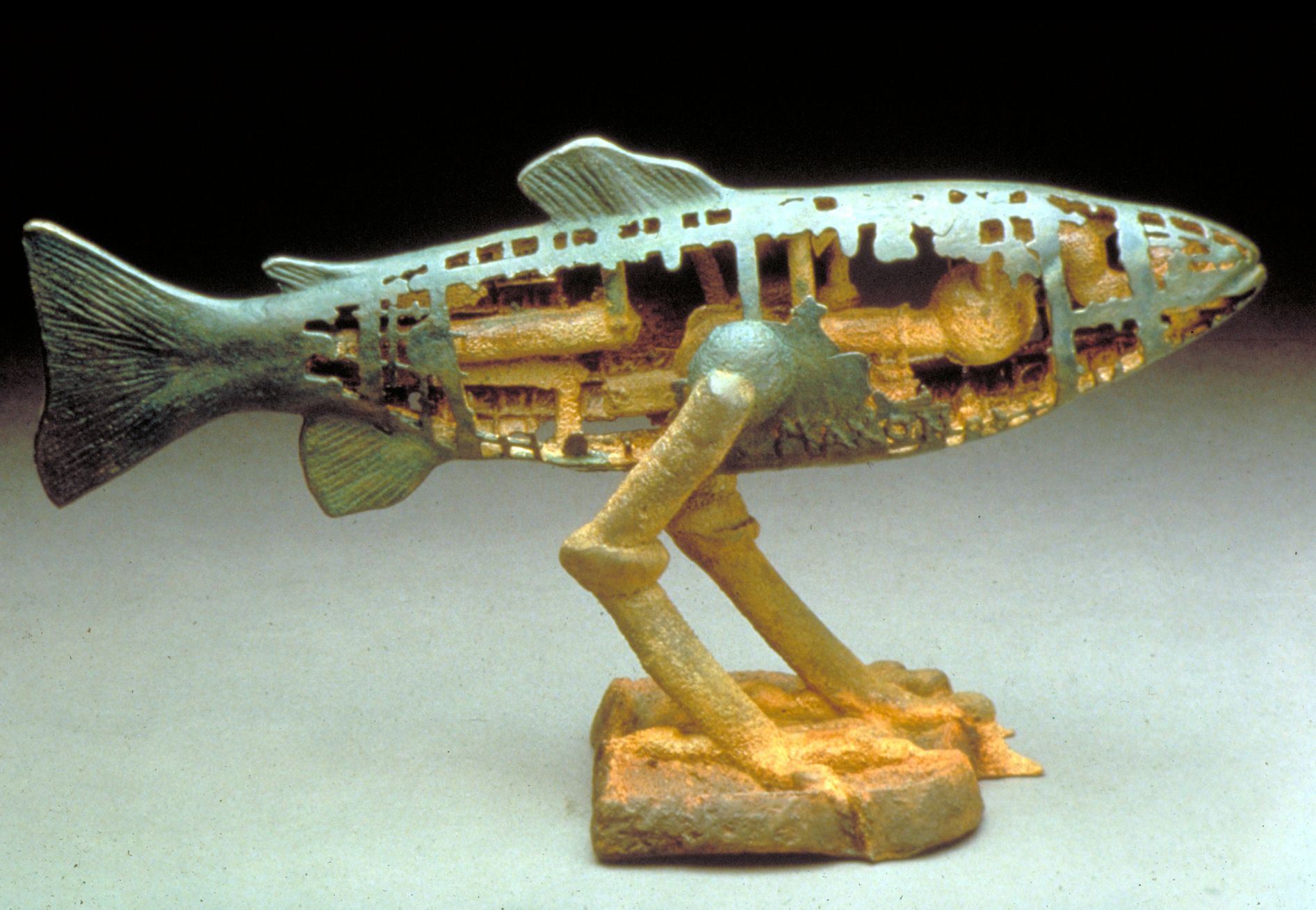 Metal fish sculpture with open body revealing gears, mounted on a small base