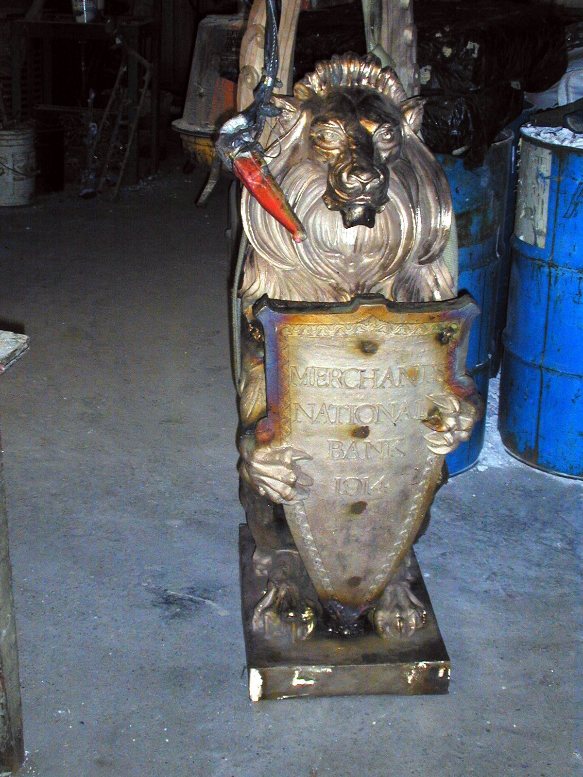 Damaged industrial machine part with a metal sculpture on top, standing in a dim workshop.