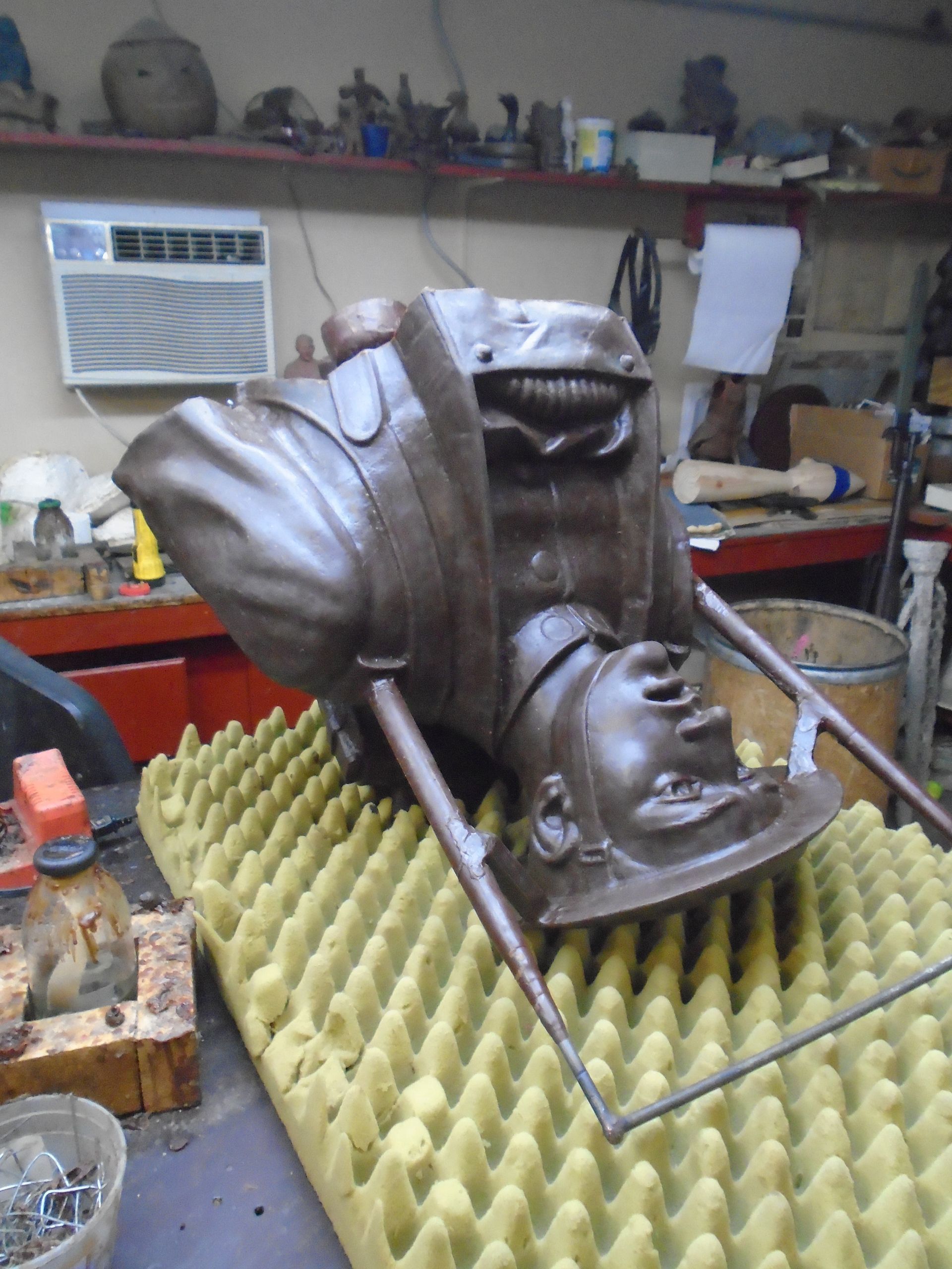 Large metal sculpture of a shoe and folded cloth on a frame in a workshop