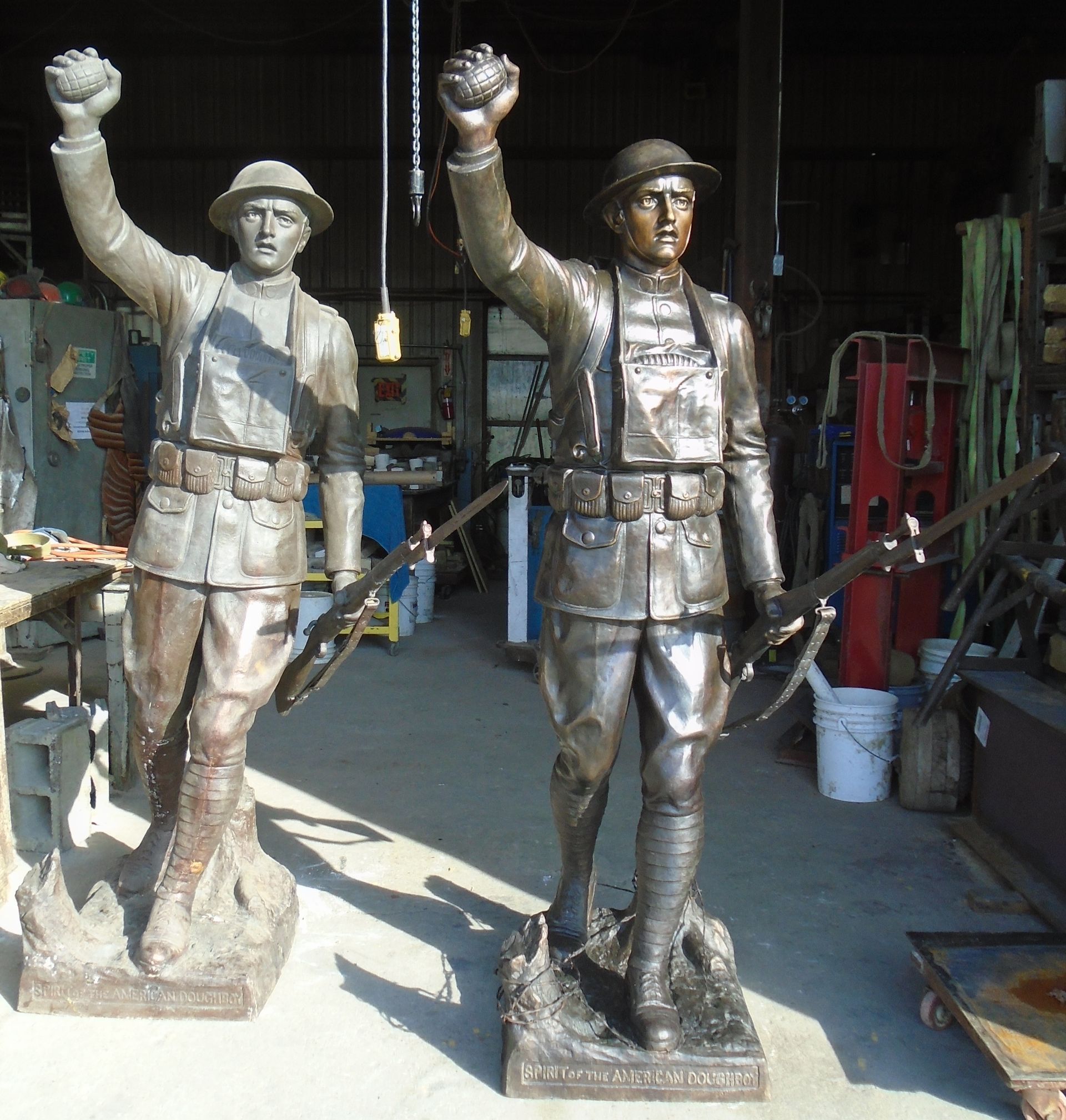 Two bronze statues of workers in a workshop, both raising one arm with fists clenched.