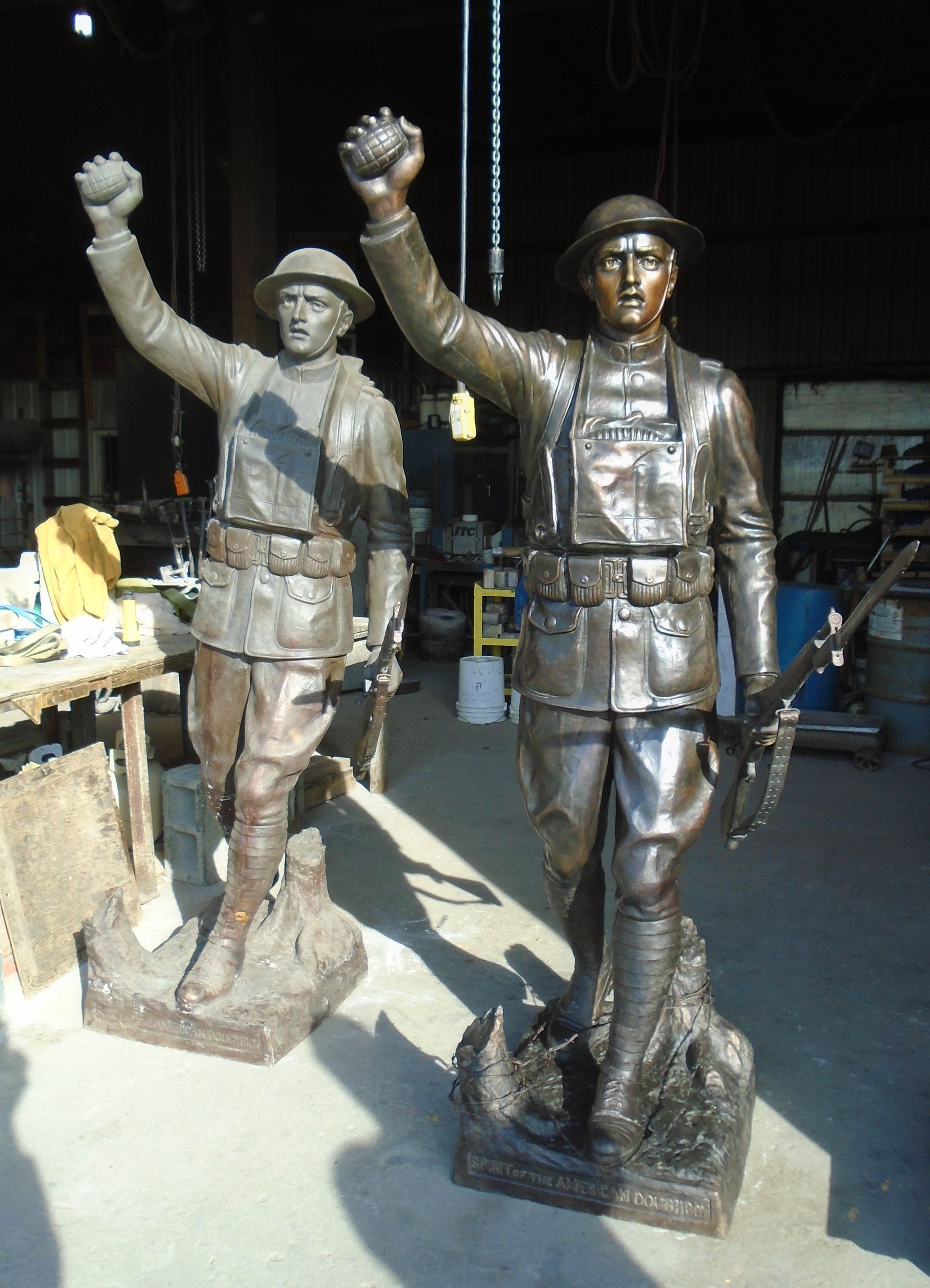 Two bronze statues of workers in hard hats, one raising a hand in a workshop setting.