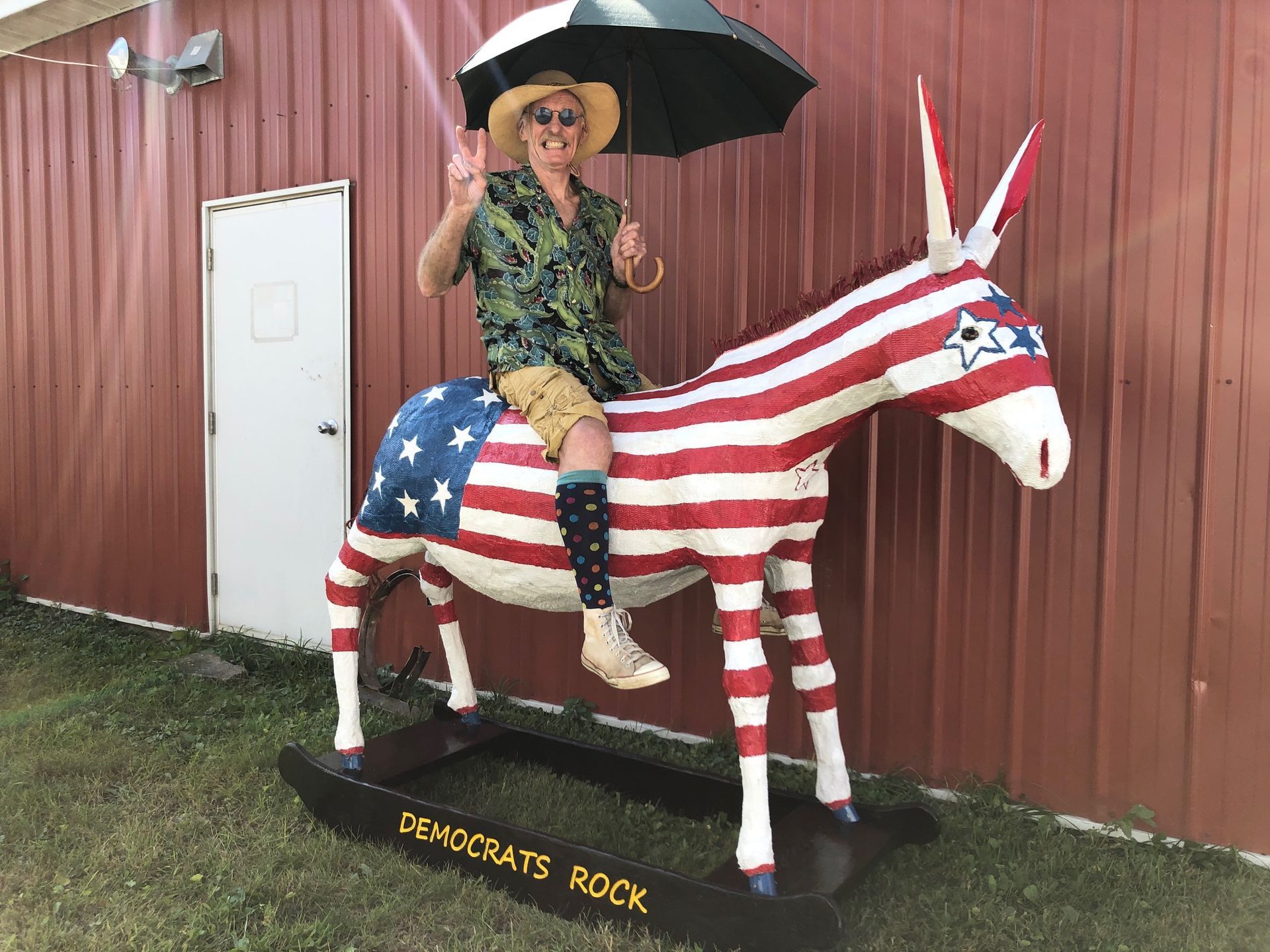 Person under an umbrella sitting on a red, white, and blue unicorn statue outside a red building