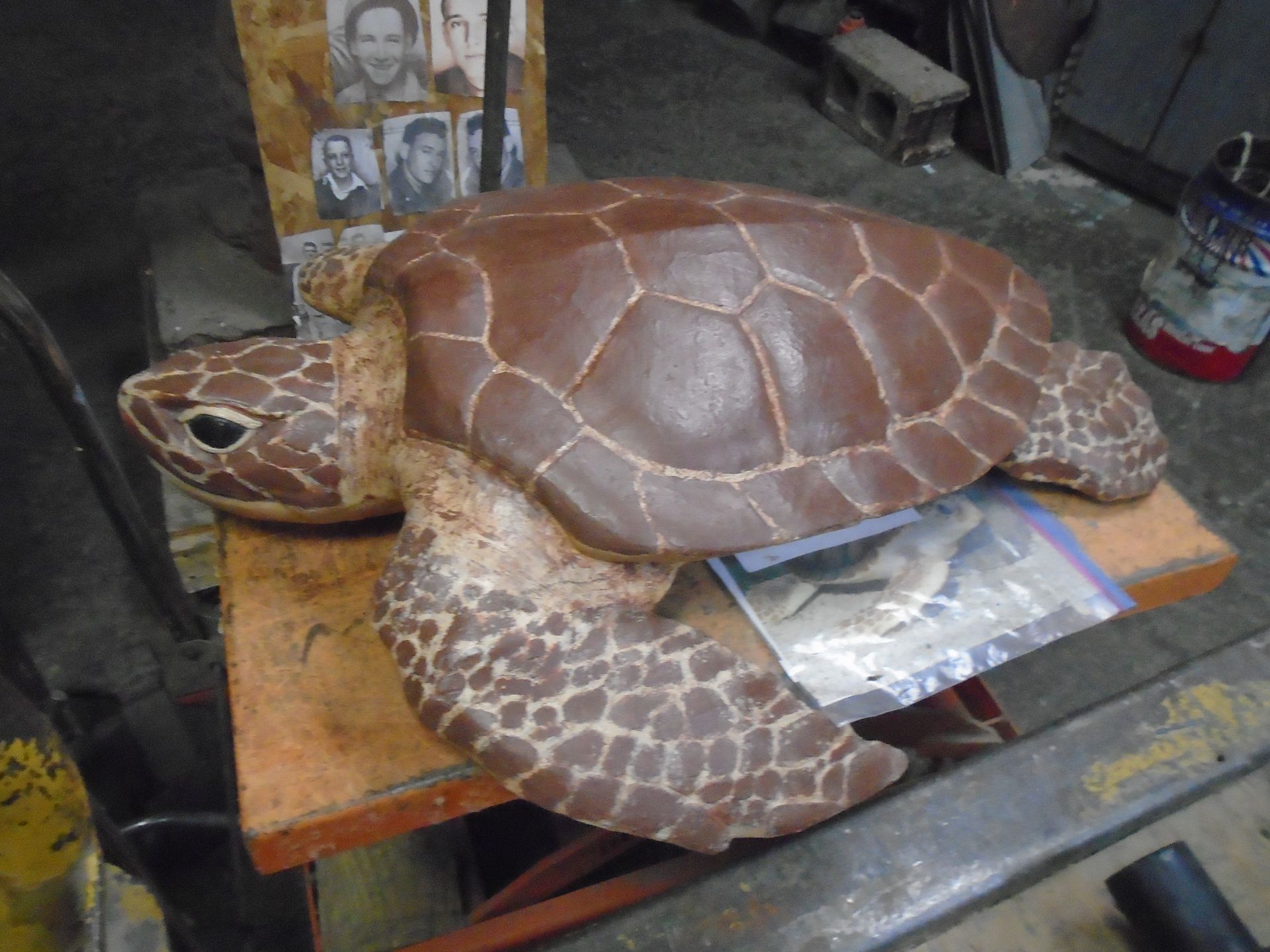 Sea turtle sculpture on a wooden table in a workshop, with another carved turtle shell nearby
