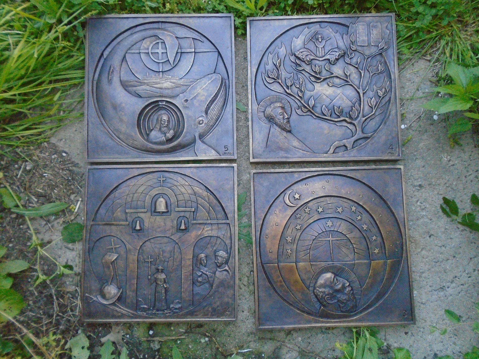 Four square stone relief panels with circular and abstract carvings on grass.