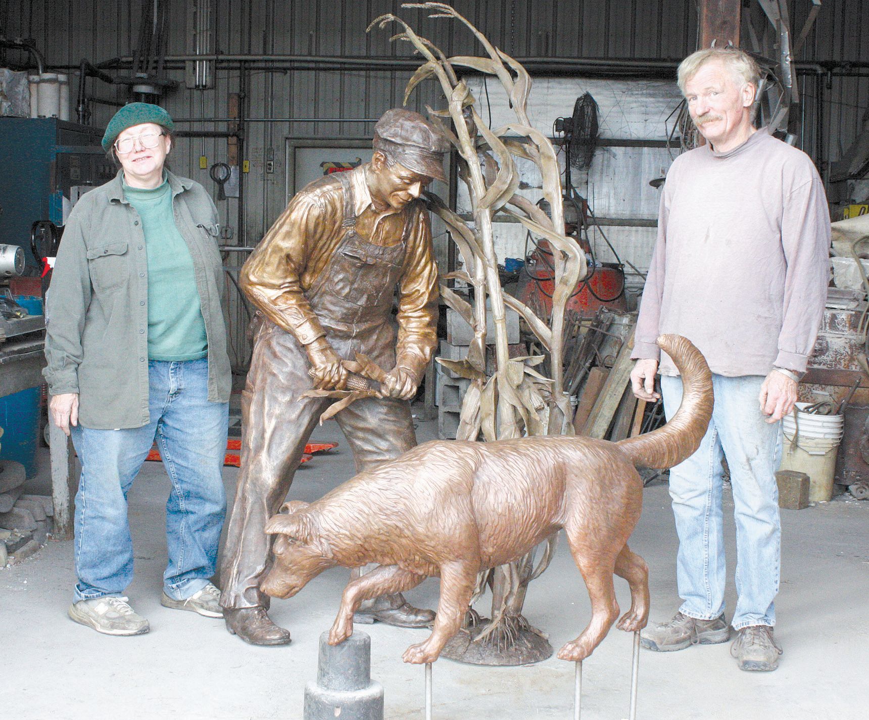 Three people stand beside bronze dog statues in a workshop.